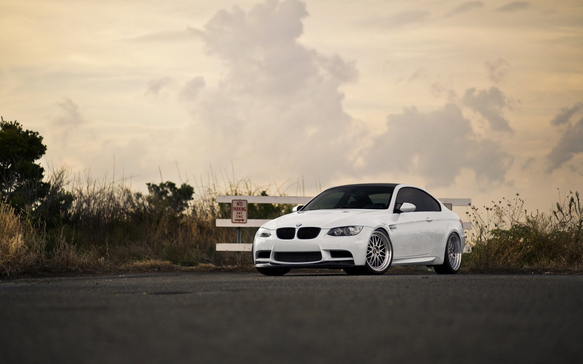 Wallpaper #ykUCm44B7YBJg1BVJKG043 A White BMW M3 Parked on an Asphalt Road Next to a White Fence