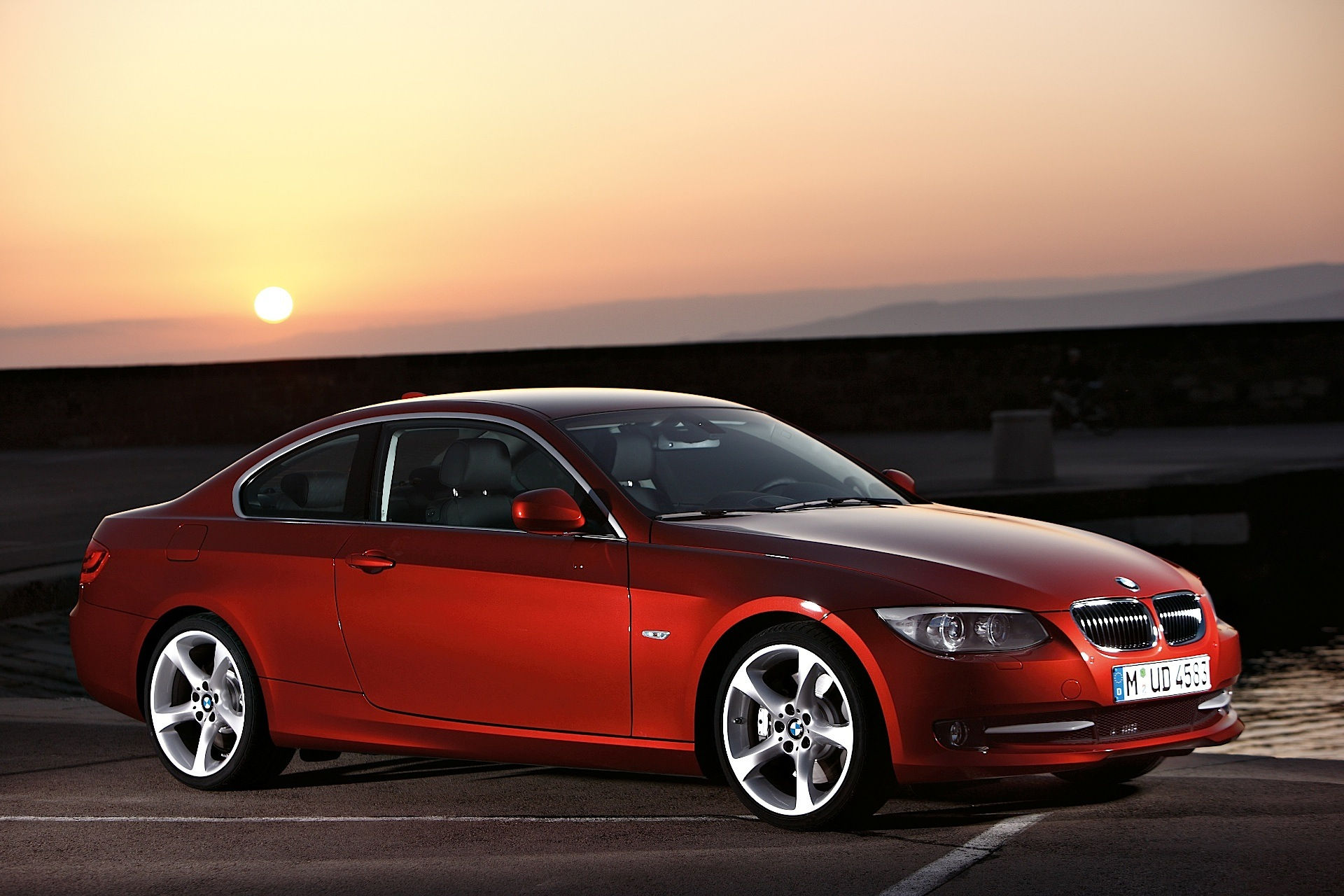 Wallpaper #lUW_oo4B7YBJg1BVBqSA16 A Red BMW Parked on a Pier with the Sun Setting in the Background