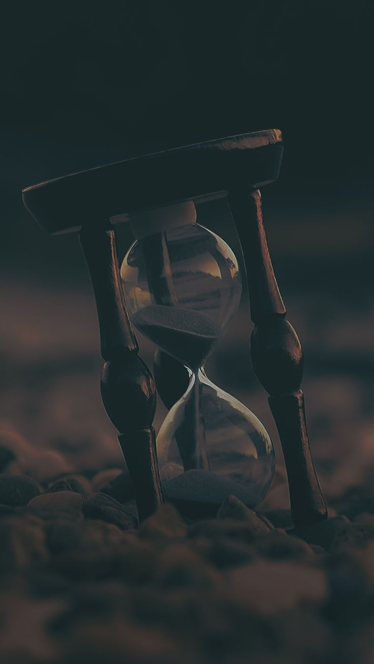 Wallpaper #57iu3JIBJvJKYCmEkfzN332 An Hourglass Sitting on Top of a Pile of Sand in Front of a Dark Background