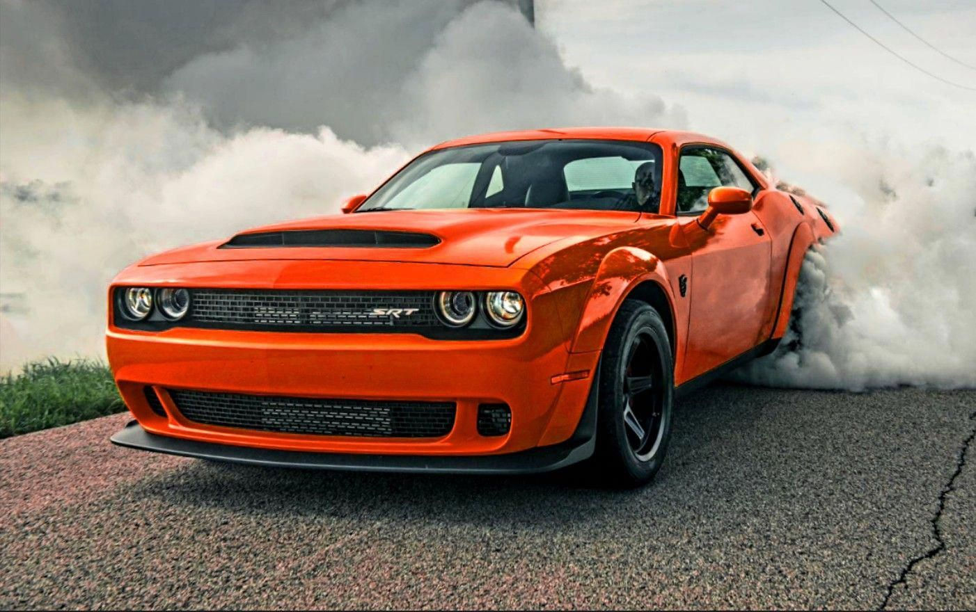 Wallpaper #-BWPso4BmMigT4UnP1FC29 A Powerful Orange Sports Car Speeds Down a Road, Leaving a Trail of Smoke Behind It