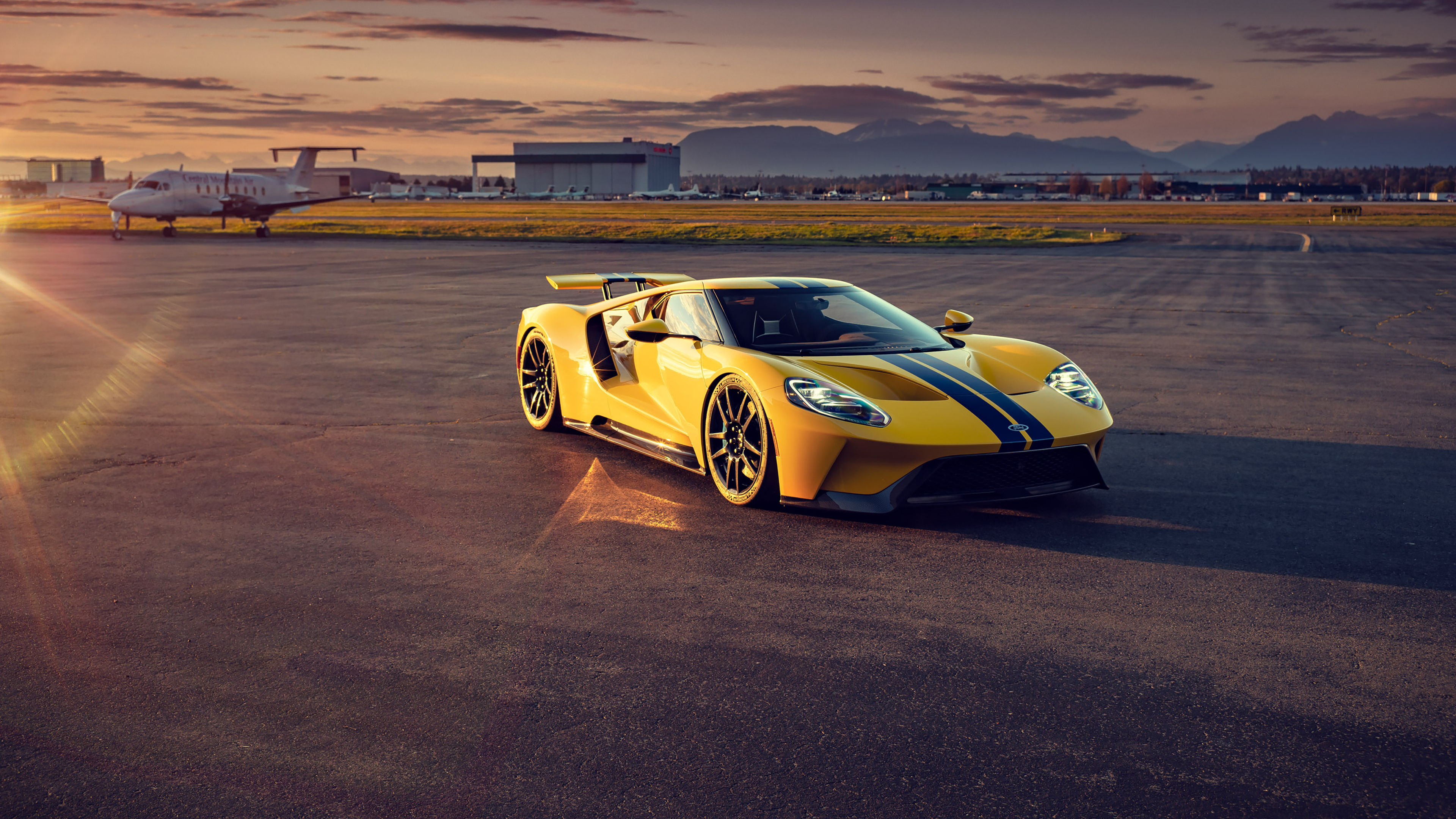 Wallpaper #z0VQl44B7YBJg1BV1qDS30 A Yellow Ford GT Supercar on an Airport Runway with a Private Jet in the Background