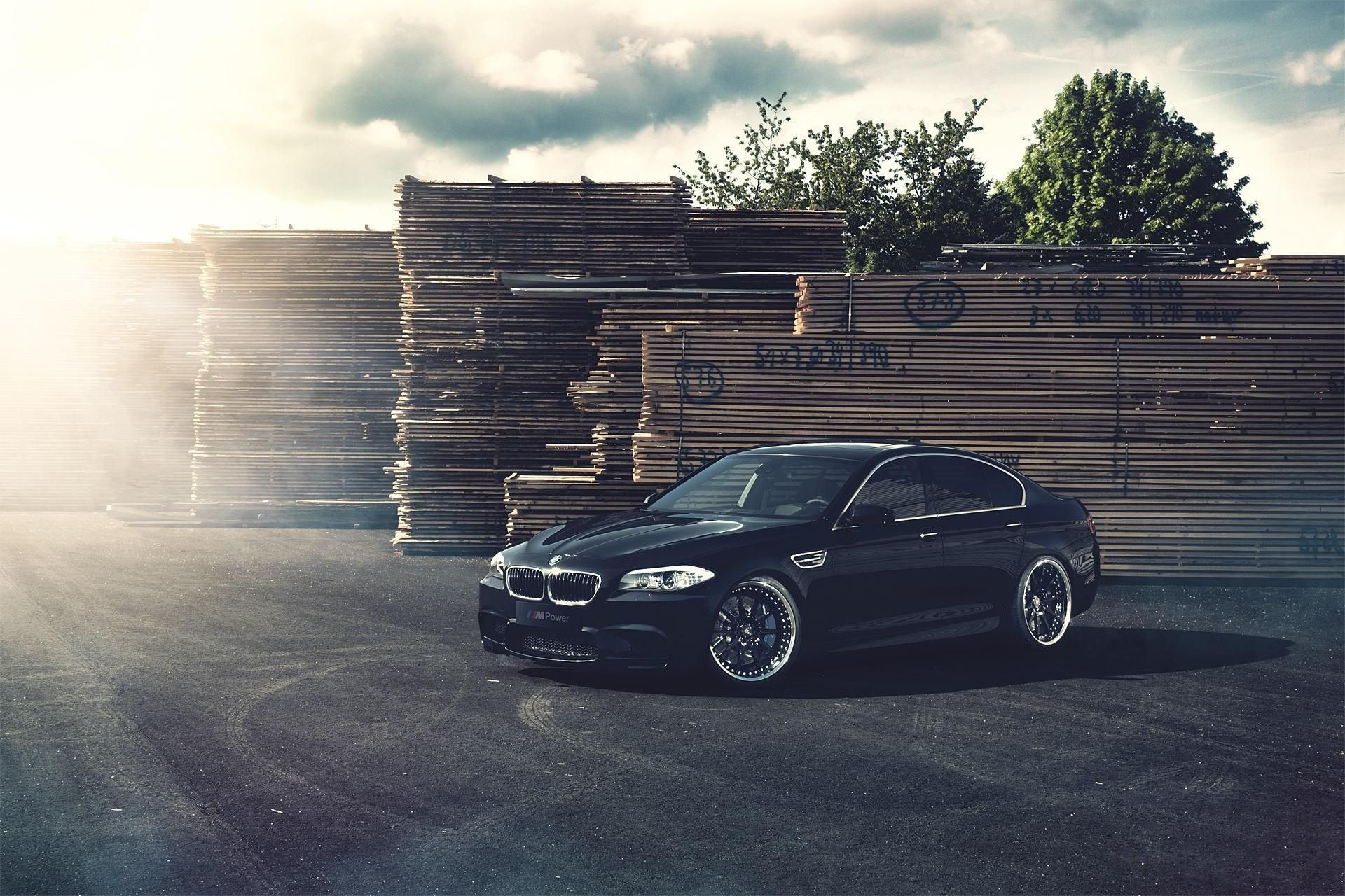 Wallpaper #z0X9ko4B7YBJg1BVTJ5P20 A Black BMW M5 Parked in Front of a Stack of Lumber