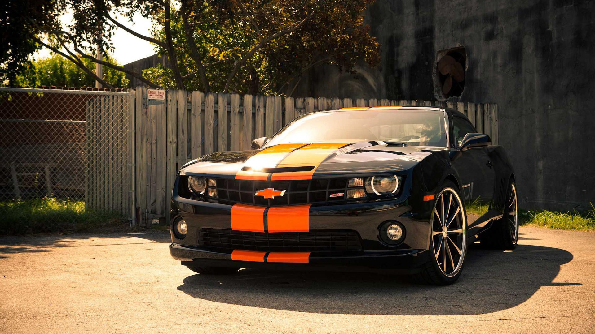 Wallpaper #A0V9jo4B7YBJg1BVFJ3F41 A Black and Orange Chevrolet Camaro Parked in Front of a Wooden Fence