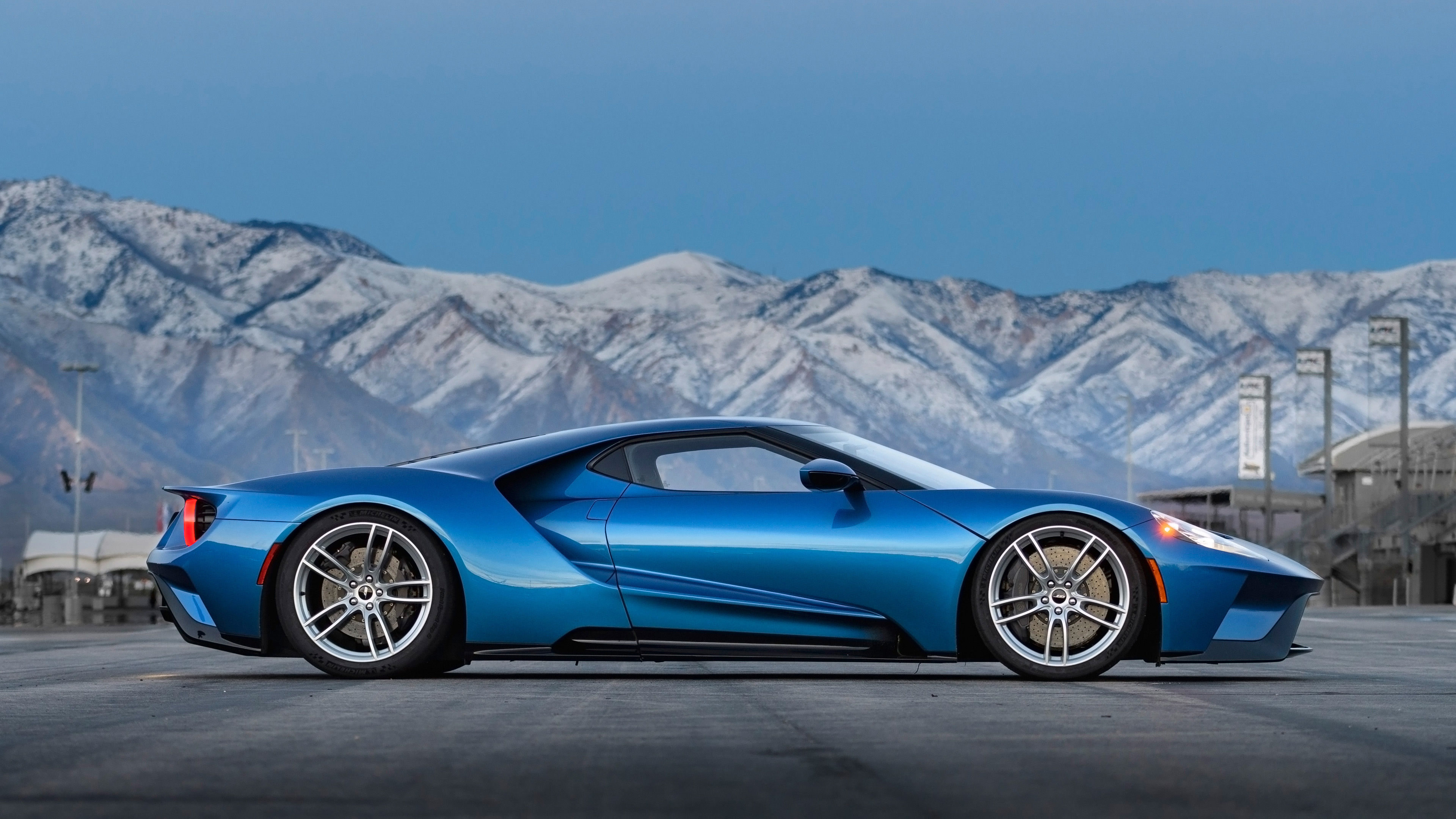 Wallpaper #z0VQl44B7YBJg1BV1qDS3 A Sleek Blue Ford GT Supercar Parked on an Asphalt Road with Snow-Capped Mountains in the Distance