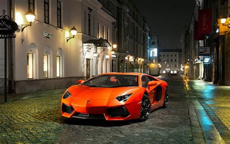 Wallpaper #YnP0fo4BFI5NbQksIxfN36 A Bright Orange Lamborghini Aventador Parked on a Cobblestone Street at Night